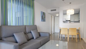 Una sala de estar moderna con un sofá gris, una mesa de centro de vidrio y un comedor con dos sillas y una mesa.