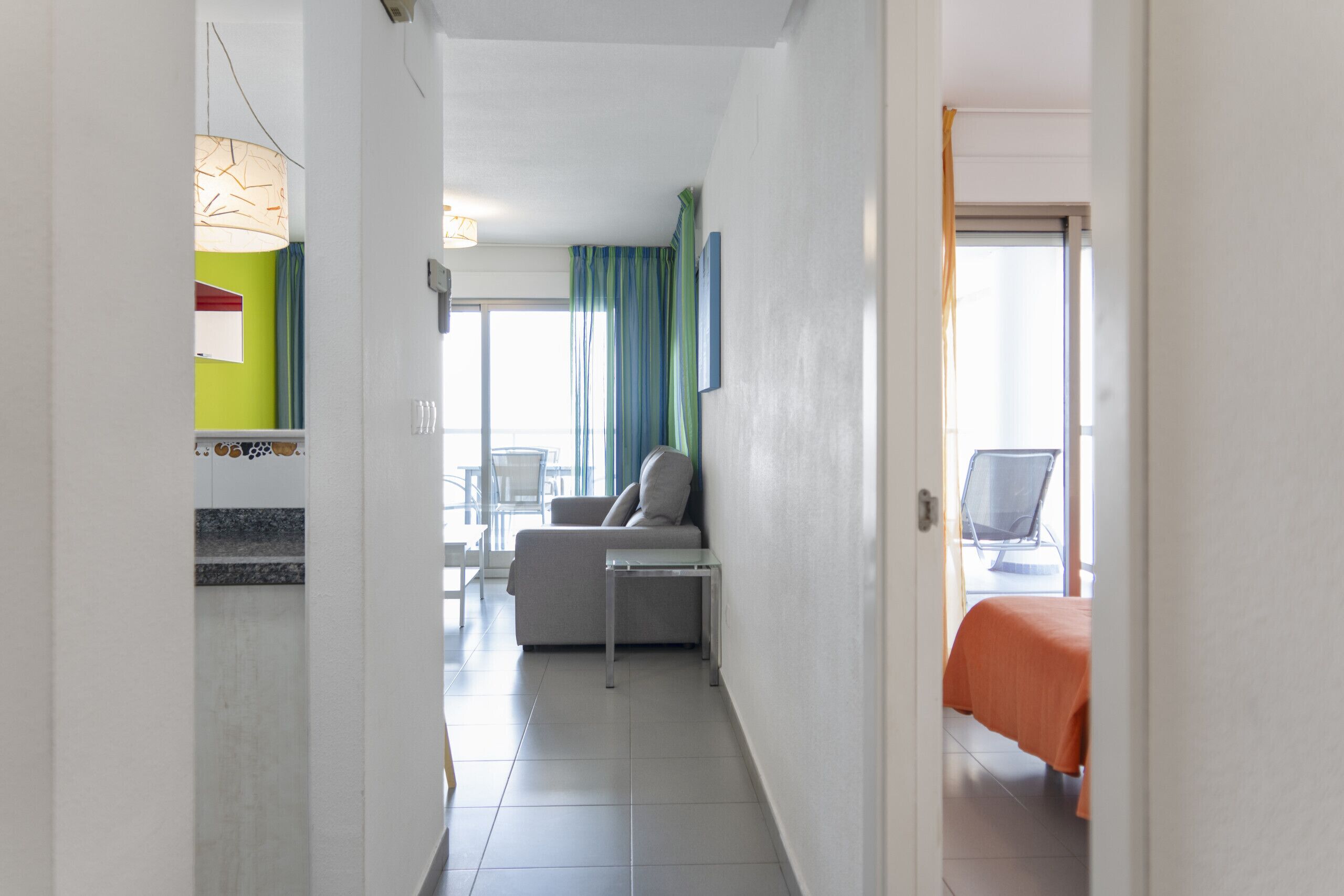 Ein Hotelgang mit einer Couch, einem kleinen Tisch und einem Bett mit orangefarbener Bettdecke.