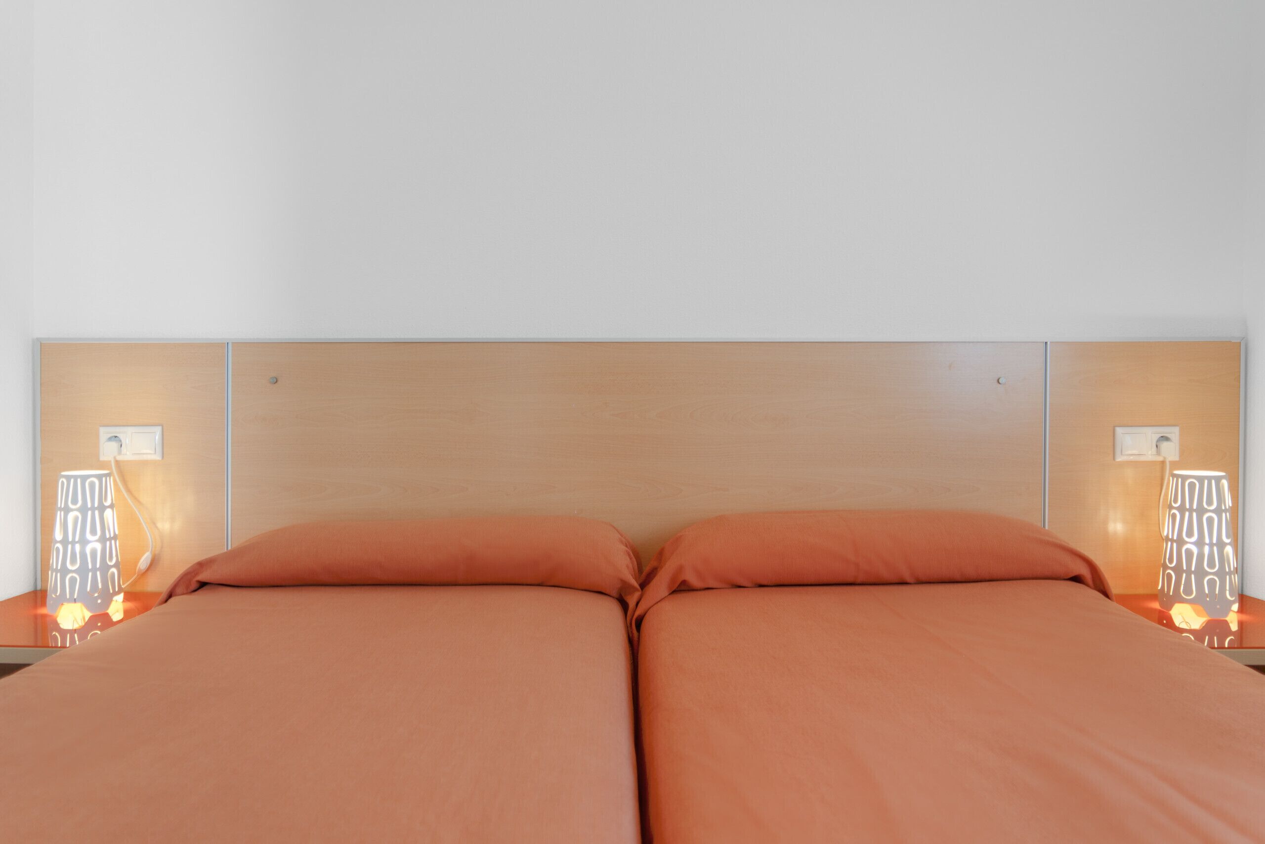 Una cama doble con almohadas a juego, cabecera de madera y lámparas de noche con diseños geométricos.