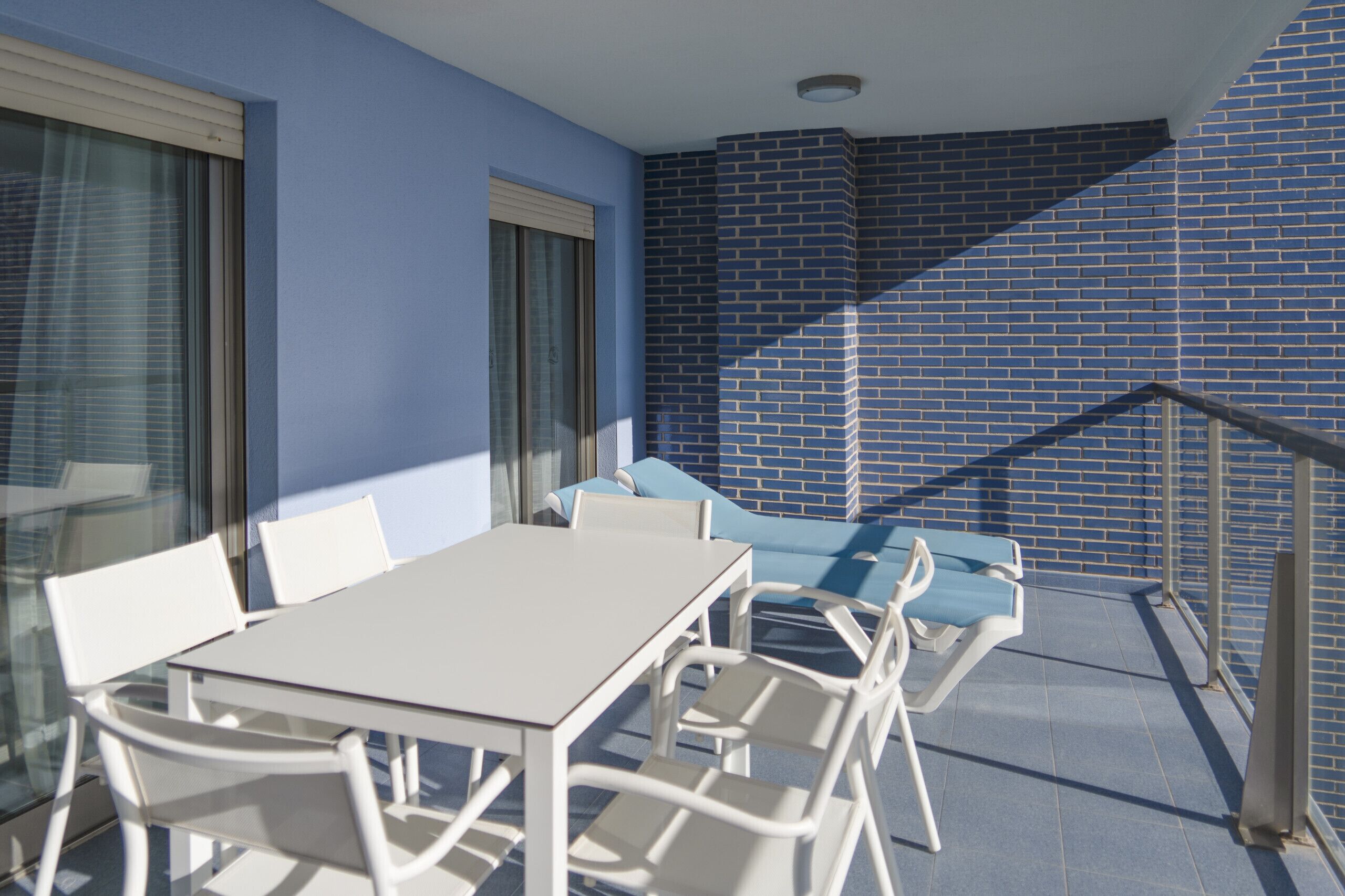 A balcony with a white table and chairs, a blue sofa, and a brick wall.
