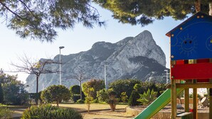 Un terrain de jeux avec un toboggan, entouré d’arbres et avec une montagne en arrière-plan.