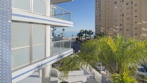 A modern building with a glass balcony overlooking a street and a body of water.
