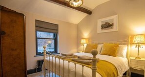 Un dormitori amb un llit, làmpades de nit, una finestra, un radiador i un quadre a la paret.