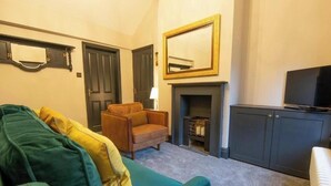 A 2 bed apartment with a green sofa, a brown armchair, a television, a fireplace, and a cabinet. - Heart of Macclesfield 2 Bedroom Grade II Apartment (Macclesfield)