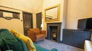 A 2 bed apartment with a green sofa, a brown armchair, a television, a fireplace, and a cabinet.