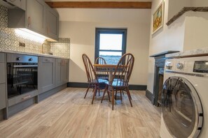 A compact kitchen with a dining table, chairs, a built-in oven, and a washing machine. - Heart of Macclesfield 2 Bedroom Grade II Apartment (Macclesfield)