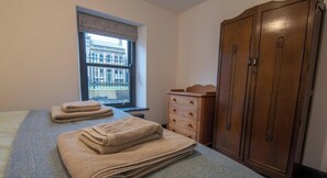 A 2 bed apartment with a large window, a wardrobe, and a bed with folded towels.