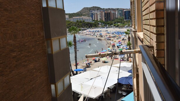 Uitzicht op een strand met parasols en mensen vanuit een hoog gebouw.