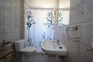 Une salle de bain équipée de toilettes, d’un lavabo et d’un rideau de douche orné d’un motif corallien.