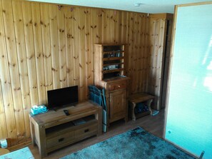 Ein Zimmer mit Holzwandverkleidung, einer Holz-Unterhaltungsanlage mit Flachbildfernseher, einem kleinen Tisch und einem blauen Teppich.