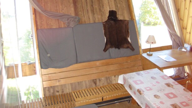 Una cabaña de madera con una cama, una mesa con una lámpara y una ventana con cortinas.