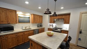 A modern kitchen with wooden cabinets, a central island, a microwave, a toaster, and a stove. - Walter Lake Area, Gated Community with Pool (Bass Lake)
