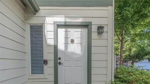 Une porte d’entrée blanche avec un encadrement vert, une petite fenêtre avec des stores et une boîte aux lettres sur le côté gauche.
