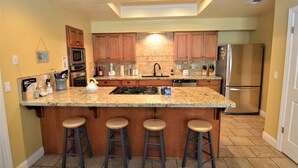 A kitchen with wooden cabinets, a granite countertop, a stainless steel refrigerator, and a built-in island with bar stools.