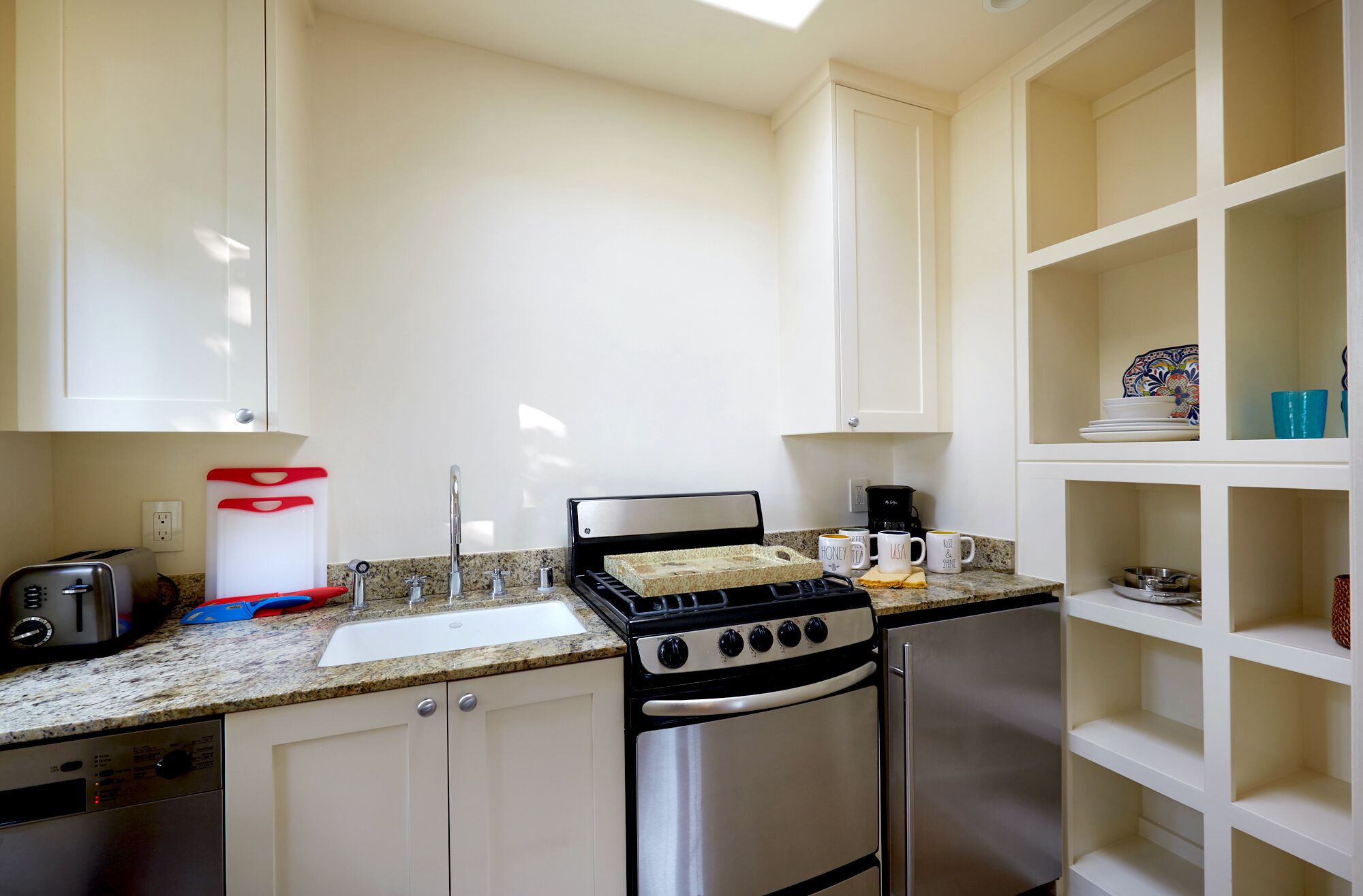 Une cuisine avec des armoires blanches, une cuisinière en acier inoxydable, un évier et une machine à café.