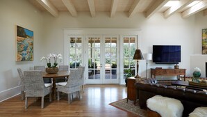Amplia sala de estar con techo de madera, comedor con sillas de mimbre, sofá de cuero y televisor en la pared.