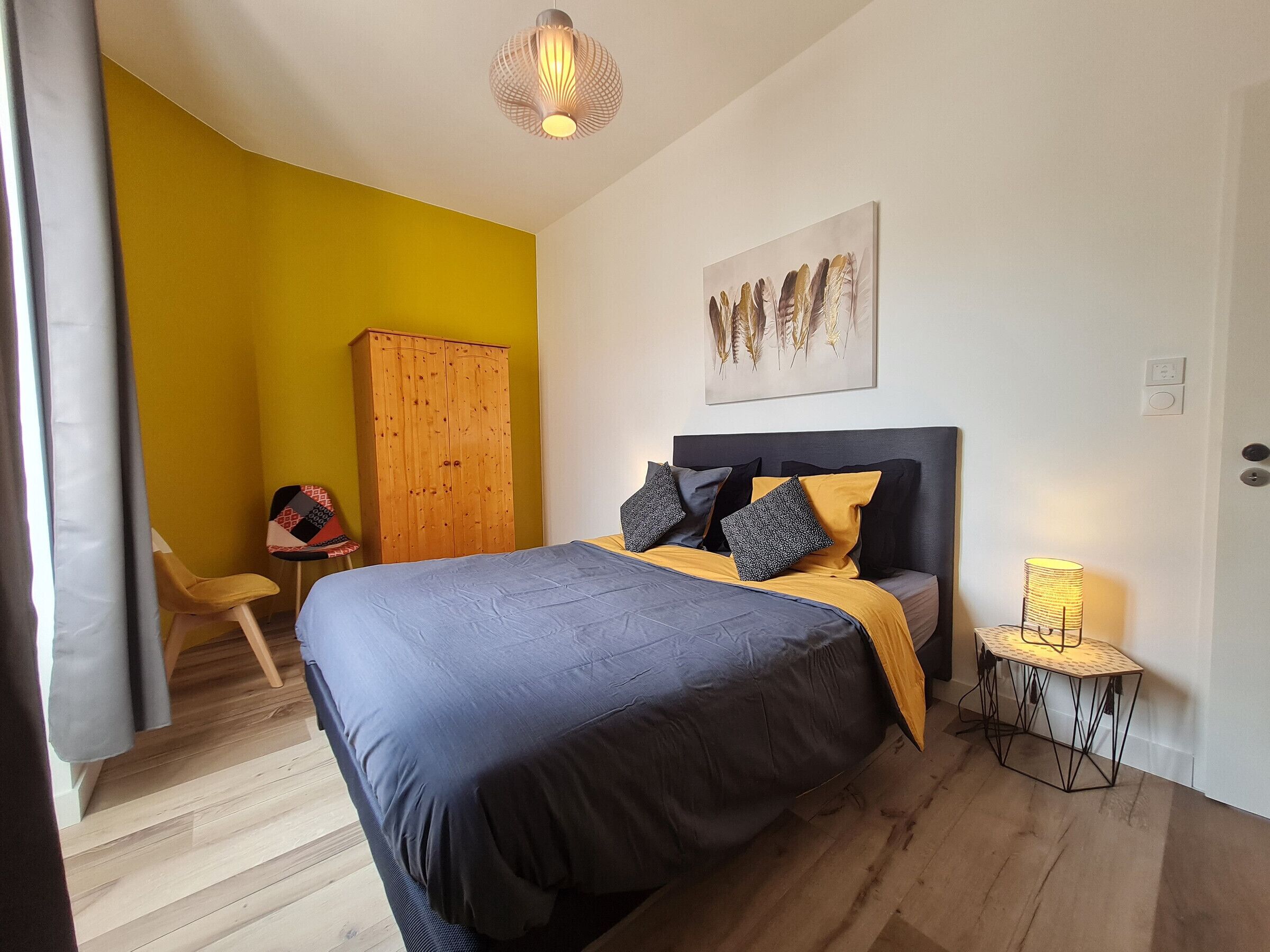Ein Schlafzimmer mit Bett, Kleiderschrank, Stuhl, Lampe und einem Bild an der Wand.