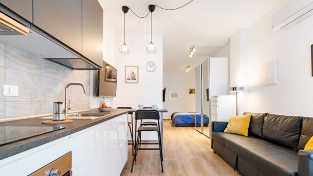 A modern kitchen with a central island, a dining area with a table and chairs, and a living area with a sofa and cushions.