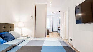 A hotel room with a bed, a TV, a lamp, and a view into the hallway.