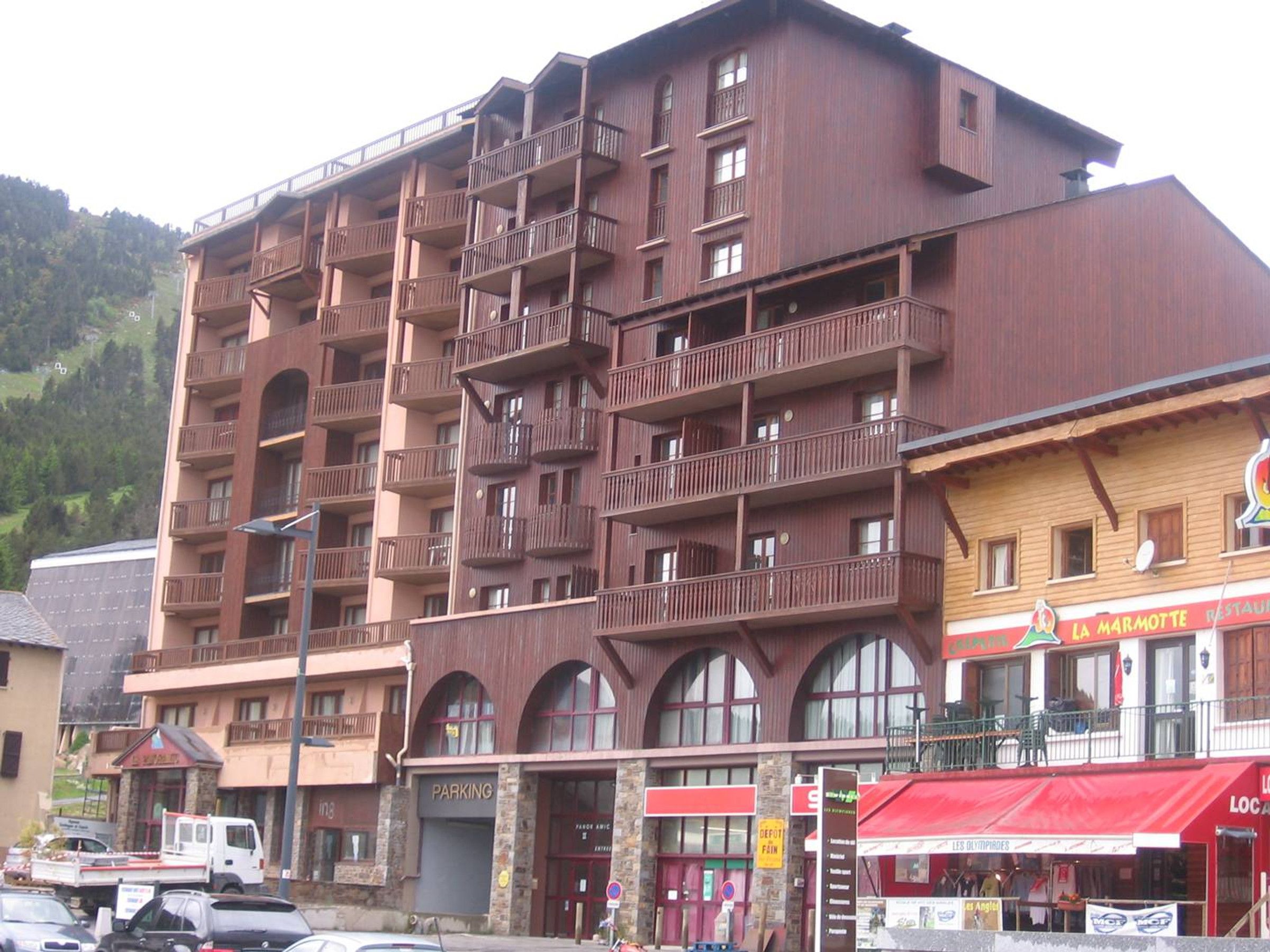 A multi-story building with balconies, a restaurant named 'La Marmotte,' and a parking area.