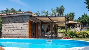 Un espace aménagé au bord de la piscine, avec un bâtiment en briques, un patio couvert et une piscine à l’eau d’un bleu limpide.