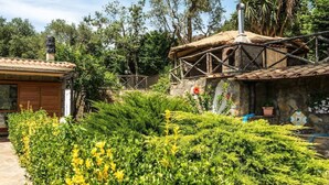 Un bâtiment rustique avec un toit en tuiles, entouré d’une végétation luxuriante et d’un mur de pierre.