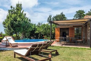 Une piscine avec des chaises longues, un patio couvert et un bâtiment en pierre avec une table et des chaises.