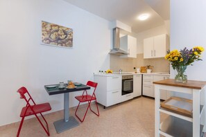 Une cuisine compacte avec des meubles blancs, une table à manger avec des chaises rouges et un petit four.