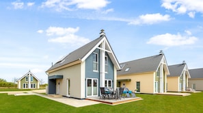 A modern residential building with a sloped roof, large windows, and a well-maintained lawn. - Vacation home Lagunen Lodge in the North Sea resort - fireplace, sauna, terrace, close to the beach, m (Büsum)