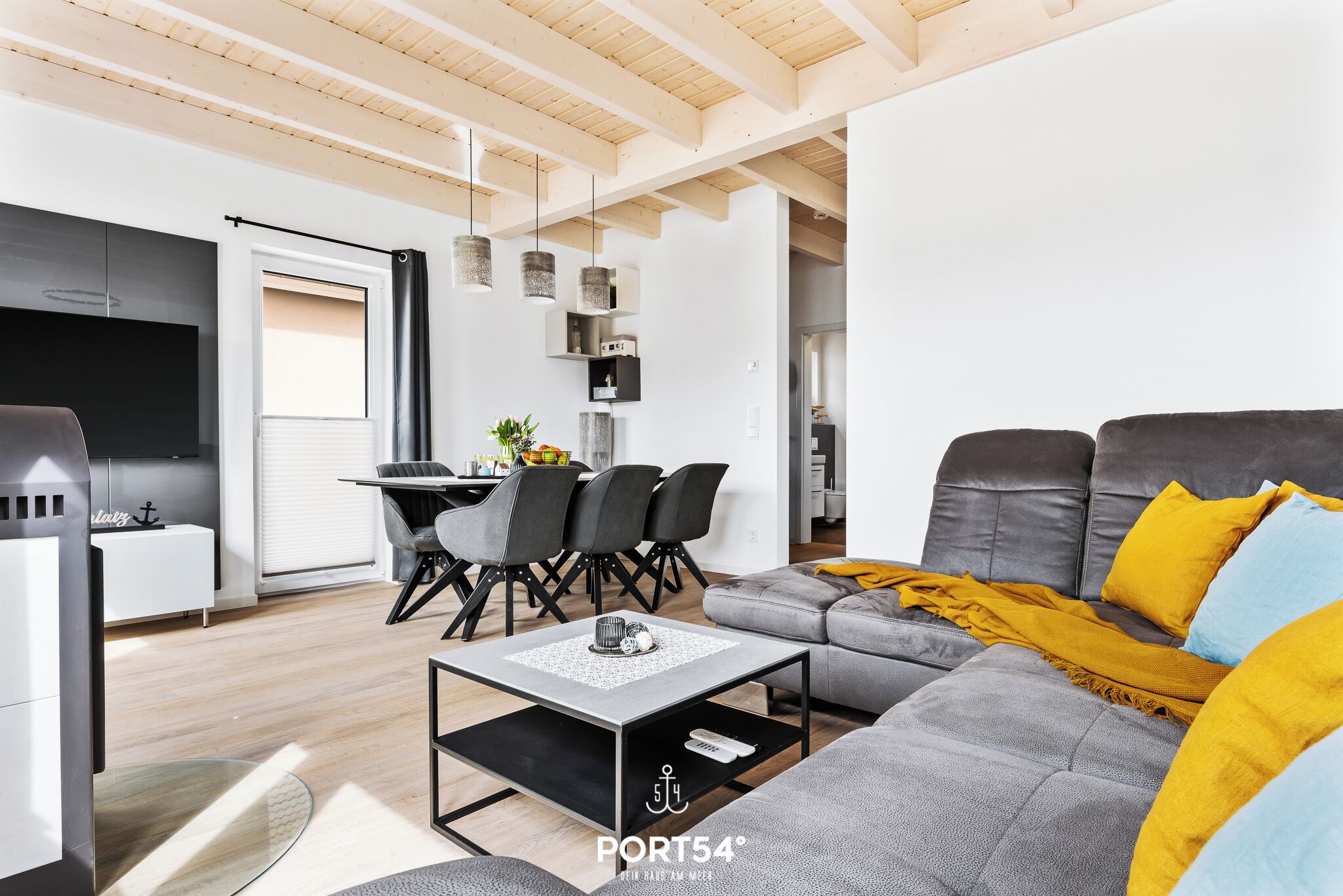 Uma sala de estar moderna com um sofá cinzento, um cobertor amarelo e uma área de jantar com cadeiras pretas e uma mesa.