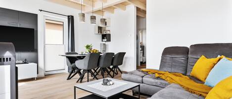 Uma sala de estar moderna com um sofá cinzento, um cobertor amarelo e uma área de jantar com cadeiras pretas e uma mesa.