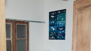 Un lit bien fait, recouvert d’une couverture rose, une armoire en bois, un tableau accroché au mur et une porte en bois.