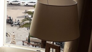 Une lampe posée sur un pied en bois, près d’une fenêtre donnant sur une rue où sont garées des voitures et où se trouve un passage piéton.