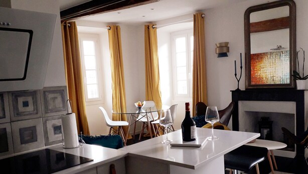Un espace repas moderne avec une table blanche, des chaises et une bouteille de vin.