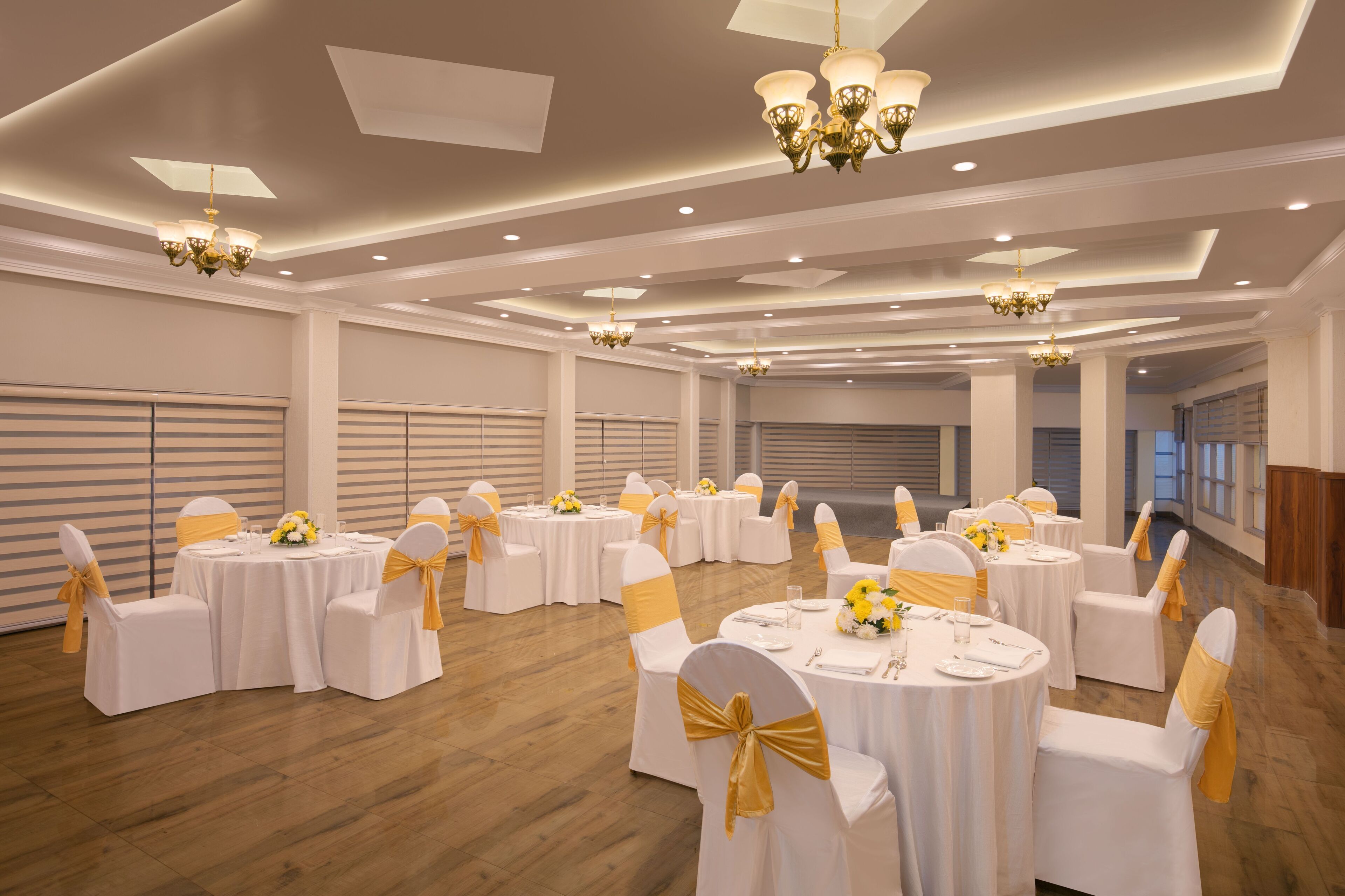 Un amplio salón de banquetes con mesas redondas, sillas blancas con cintas doradas y candelabros.