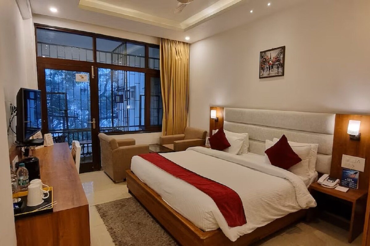 A hotel room with a large bed, a desk with a coffee maker, and a view of the outdoors through a large window.