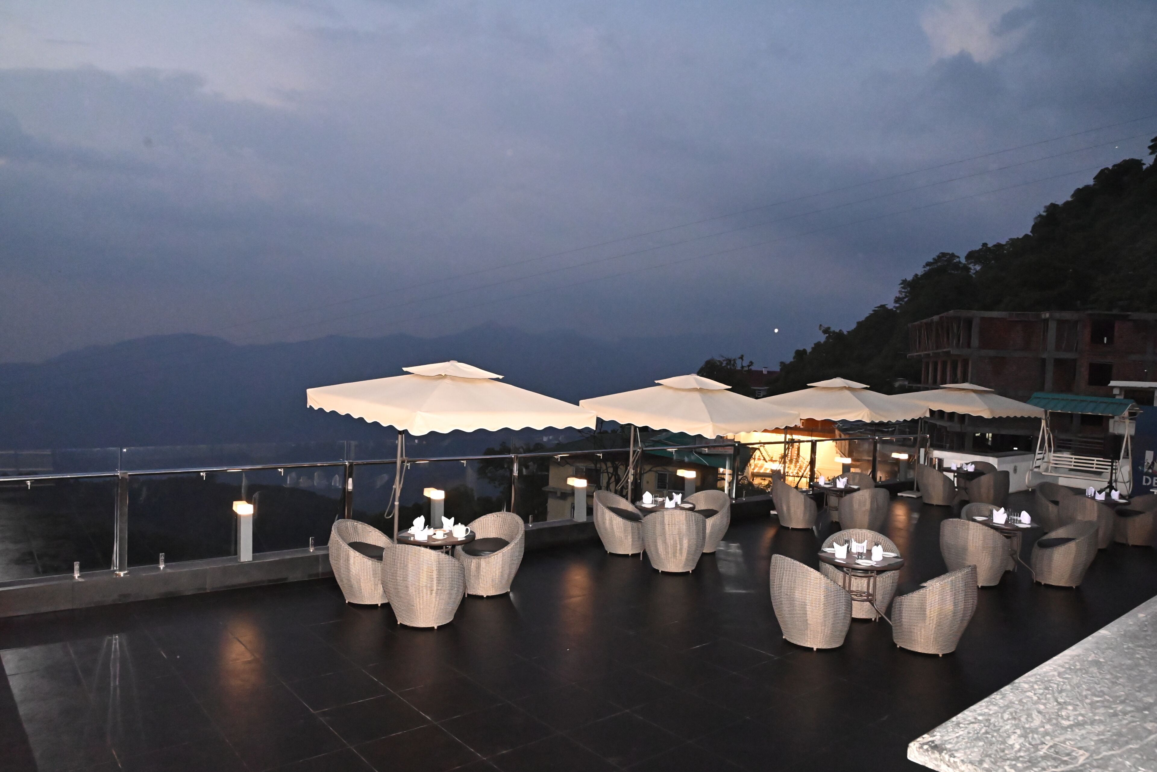 Terraza con mesas al aire libre y sombrillas, con vistas a un cuerpo de agua y montañas.