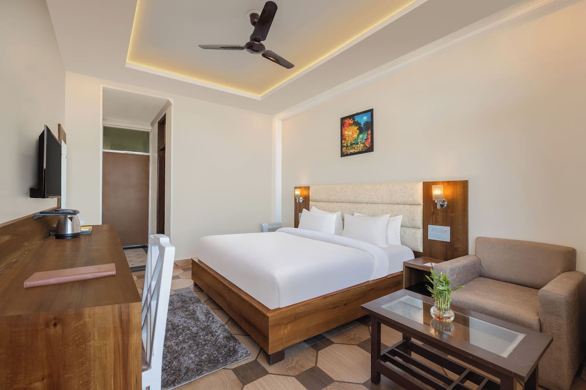 A hotel room with a bed, a desk, a chair, a ceiling fan, and a painting on the wall.