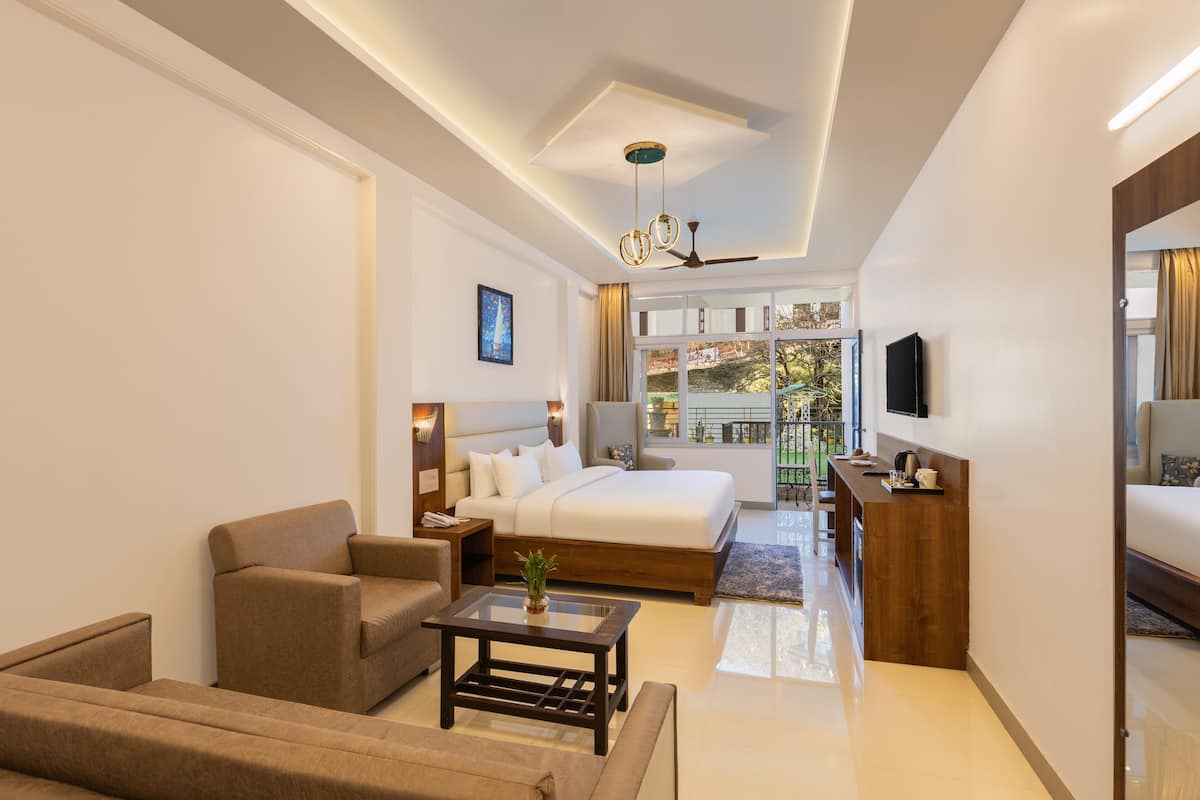 A modern hotel room with a large bed, a sofa, a coffee table, a TV, and a balcony with a view.