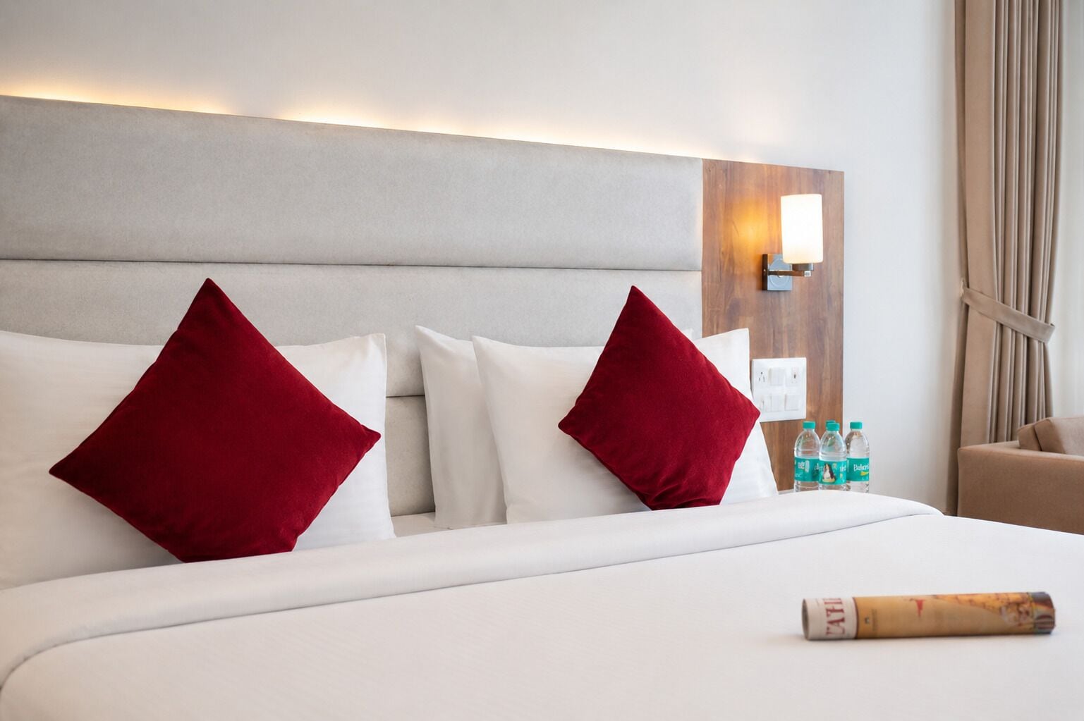 A hotel room with a bed, pillows, a lamp, and a bottle of water.
