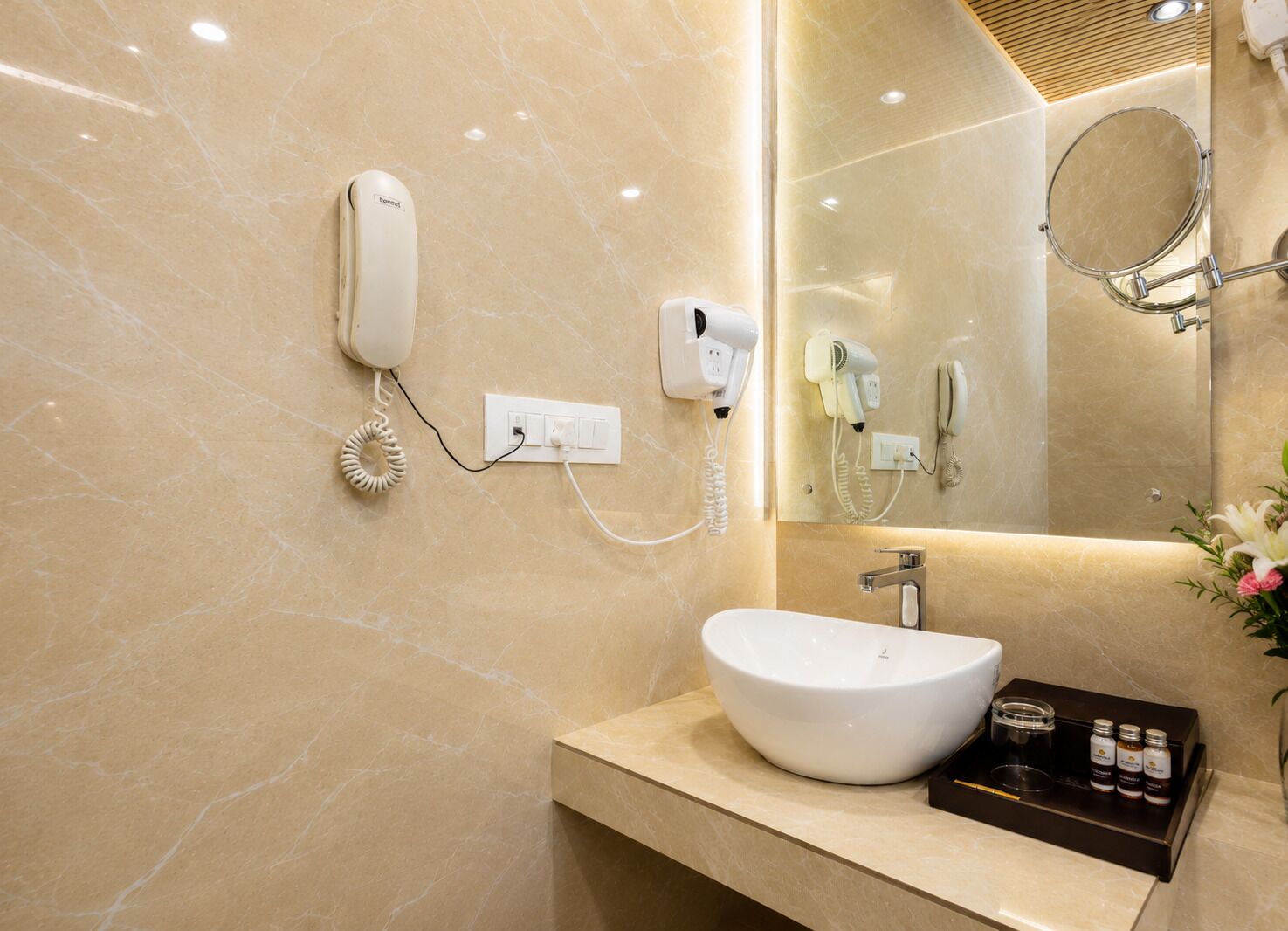 Une salle de bain avec un lavabo blanc, un miroir, un sèche-cheveux et un téléphone fixé au mur.