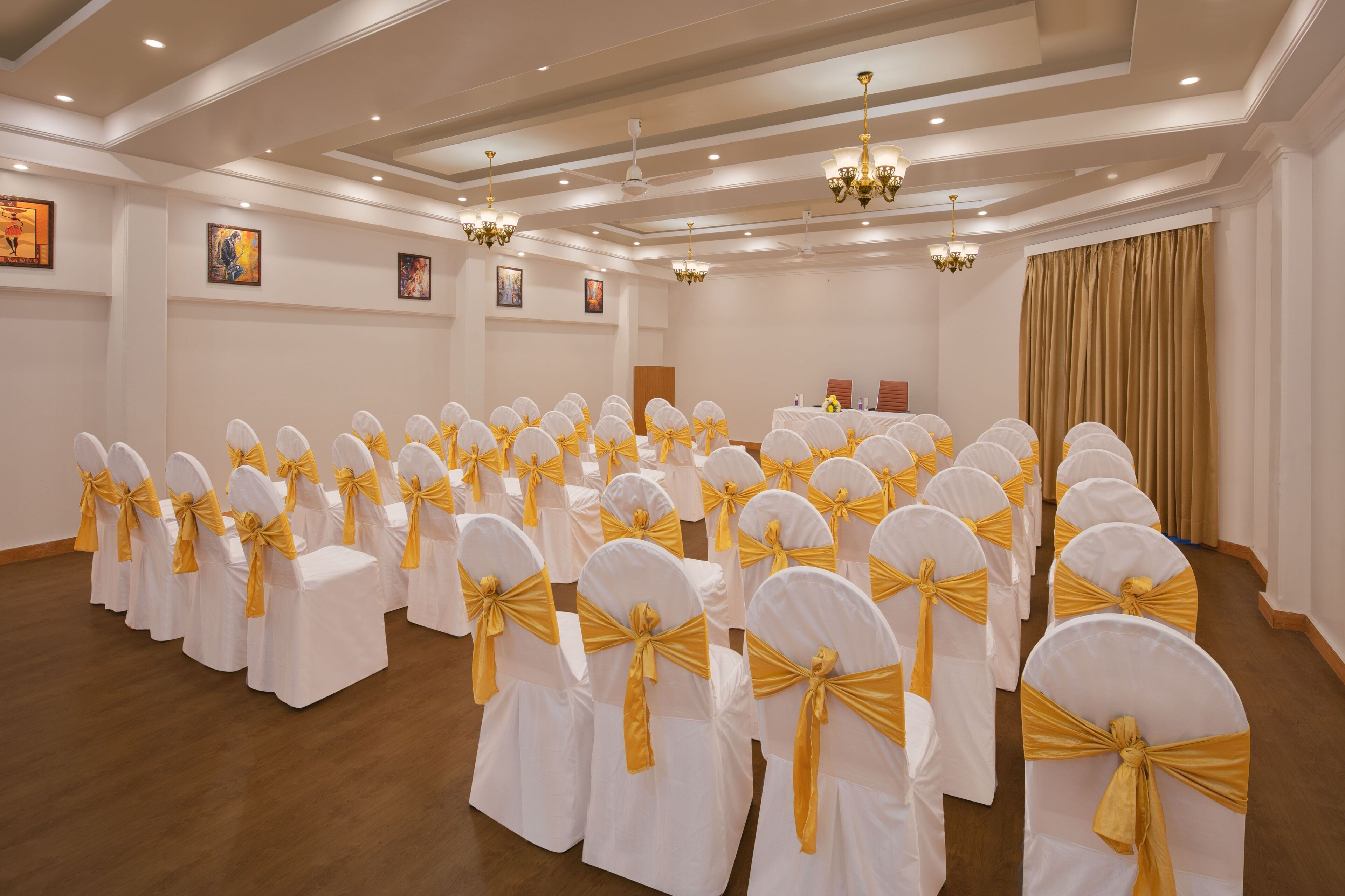 A conference room with rows of white chairs with yellow sashes, a stage with a podium, and ceiling lights.