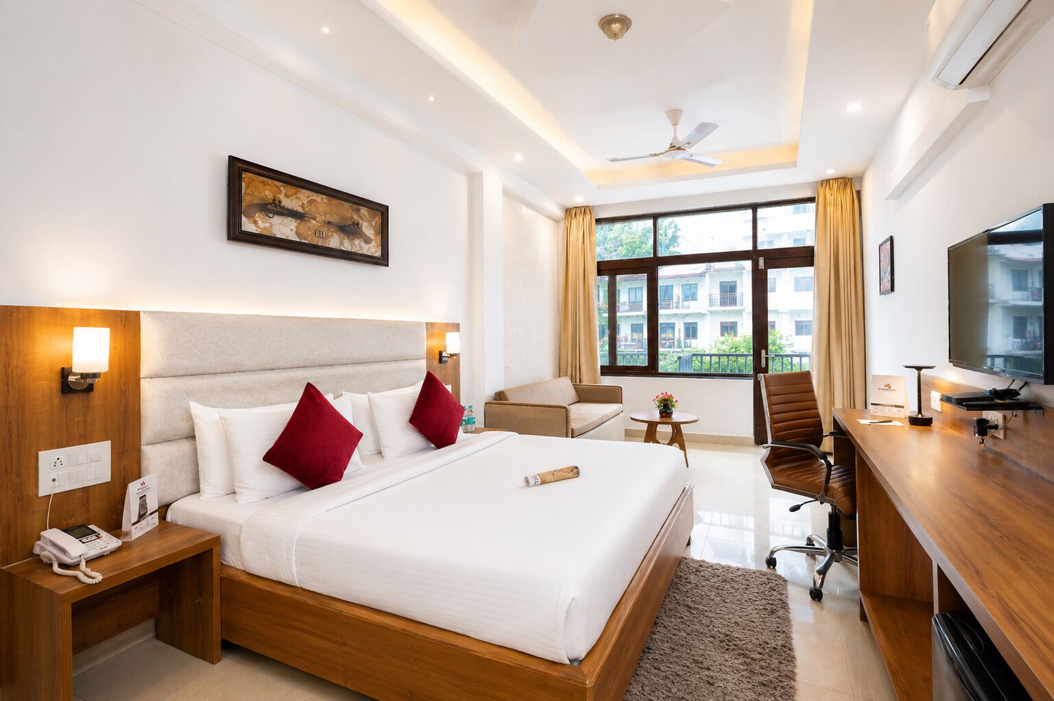 A hotel room with a large bed, a desk, a chair, a television, and a window with a view of buildings.