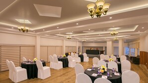 A banquet hall with round tables, white chairs, and chandeliers. - Pride Ashiyana Resort Mussoorie (Dehradun)