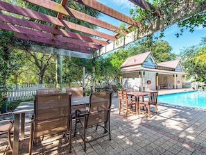 An outdoor patio with a pool, wooden furniture, and a covered seating area.