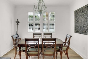 Una sala da pranzo con un tavolo rotondo, sei sedie, un lampadario e un'ampia finestra con tende.
