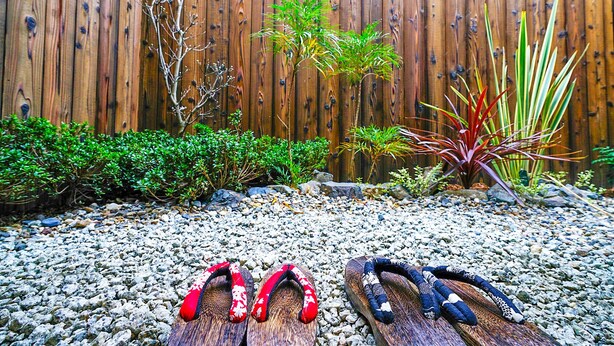 A garden with a wooden fence, various plants, and a pair of shoes on a gravel path. - INN Plus Toji Kindo (Kyoto)