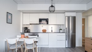 Une cuisine moderne avec des meubles blancs, un réfrigérateur en acier inoxydable, une machine à café et un coin repas avec des chaises blanches.