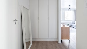 Un couloir avec une armoire blanche, une table d’appoint en bois et une vue sur un salon comprenant un canapé et un luminaire suspendu.