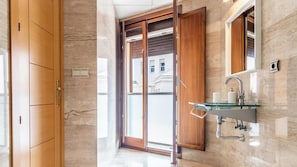 Un baño moderno con un lavabo de vidrio, armarios de madera y una puerta corrediza de cristal que da a un balcón.